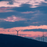 Comment fonctionne vraiment l'énergie éolienne, de la pale au compteur Parc éolien terrestre au coucher du soleil, pales en rotation sur fond de ciel orangé