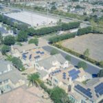 Technicien nettoyant des panneaux solaires sur un toit en pente avec brosse télescopique